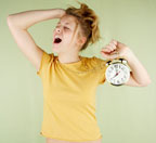 Image of a womaning stretching while holding an alarm clock and yawning
