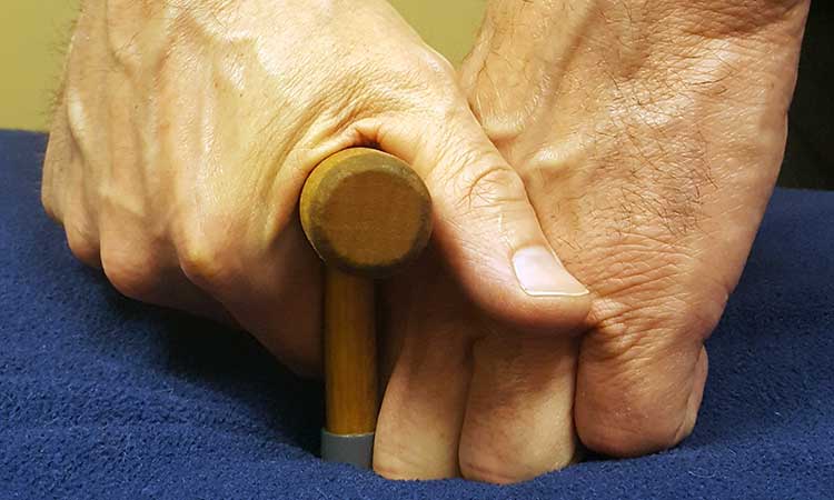 Instead of continuing to tighten your hand around the handle, you place your other hand, the non-holding hand, next to the T-bar to support it. Now you can loosen your grip because the massage tool is stabilized between both hands.