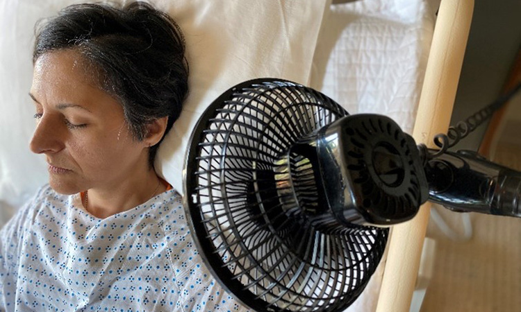 An image of a woman in a hospital gown sitting near a fan is used to illustrate the concept of COVID patients having shortness of breath.