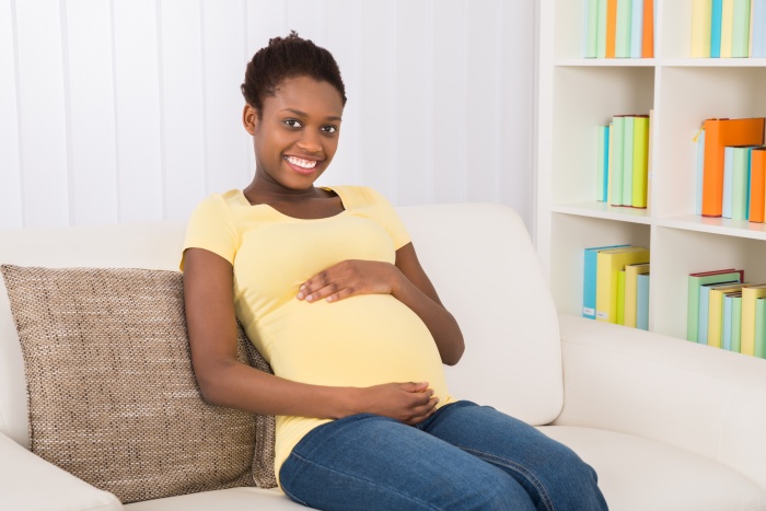 Happy Pregnant Woman Sitting On Sofa At Home