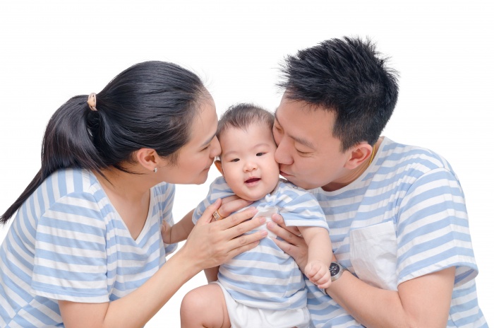 Young asian parents kissing their child isolated over white