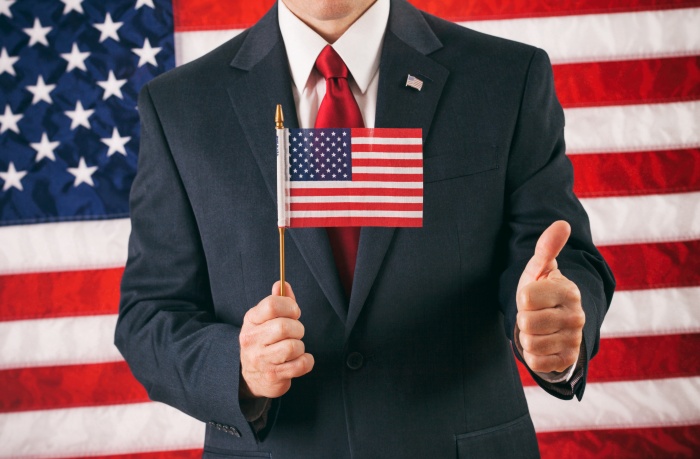 politician holding mini american flag against american flag backdrop