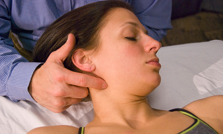 A massage therapist applies gentle pressure to a spot along the client's jawline.