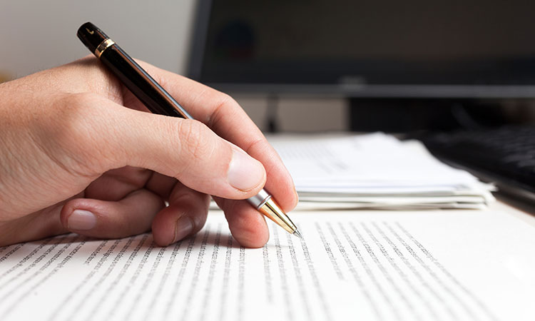 An image of a hand holding a pen and writing a report is used to illustrate the concept of writing a massage therapy case report.