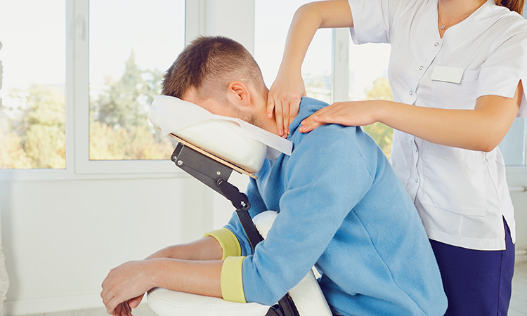 A massage therapist works on a client's shoulders and neck while he sits in a massage chair, to illustrate the concept of building your business using chair massage.