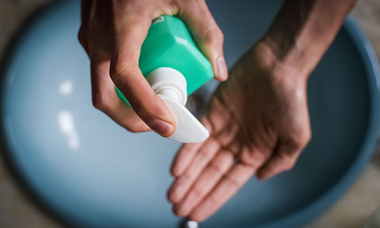 Young man cleaning hands, using hand sanitizer over sink, to prevent spreading virus. Corona virus prevention and contention measures and personal hygiene.