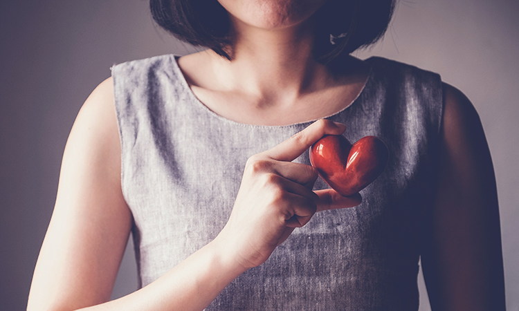 woman holding red ceramic heart over her chest.