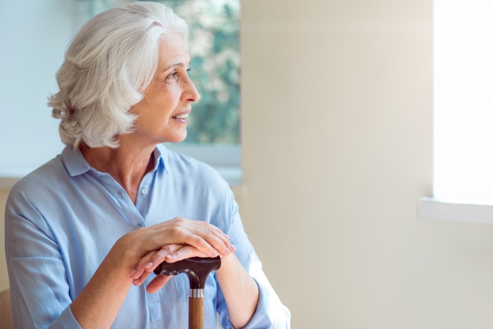 Far away with thoughts. Happy and smiling senior woman sitting with crutch and looking straight