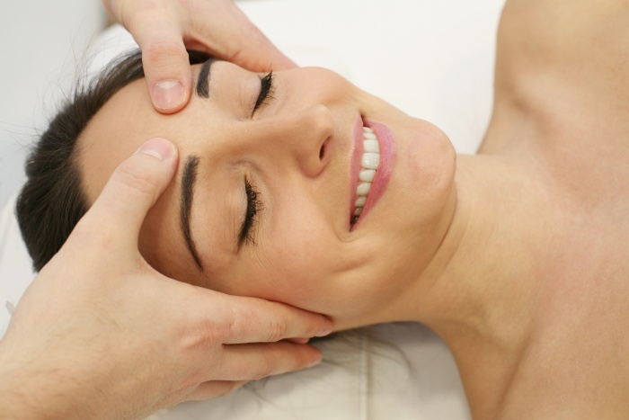 Female esthetician massaging head and face of young woman during facial.