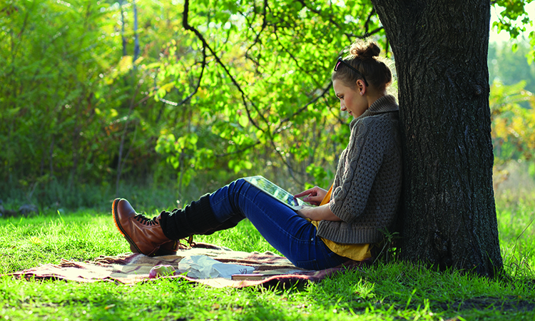 Girl leaning on a tree and using tablet computer
