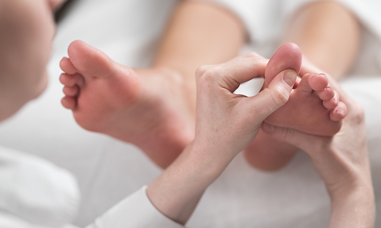 Professional female massage therapist giving reflexology massage to woman's foot.