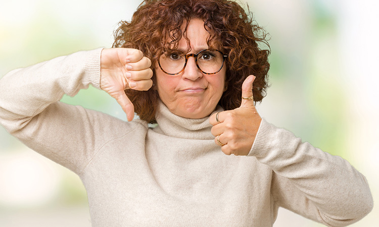 An image of a woman making a thumbs-up signal with one hand and a thumbs-down signal with the other is used to illustrate the concept of prioritizing self-care, which can often be challenging and confusing.