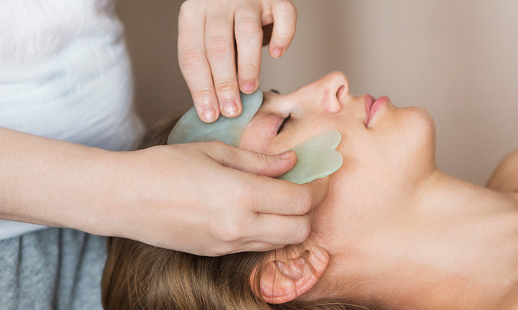 A spa therapist is shown giving a facial treatment to a client in order to illustrate the concept of this article's topic, spa trends.