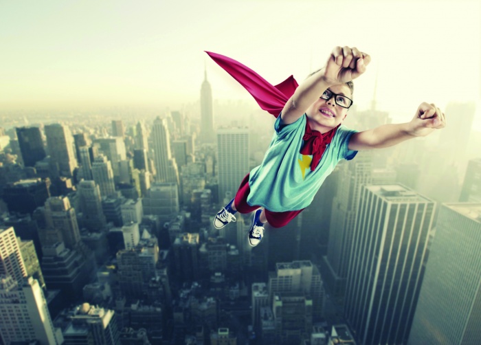 little boy with glasses as a superhero flying over city