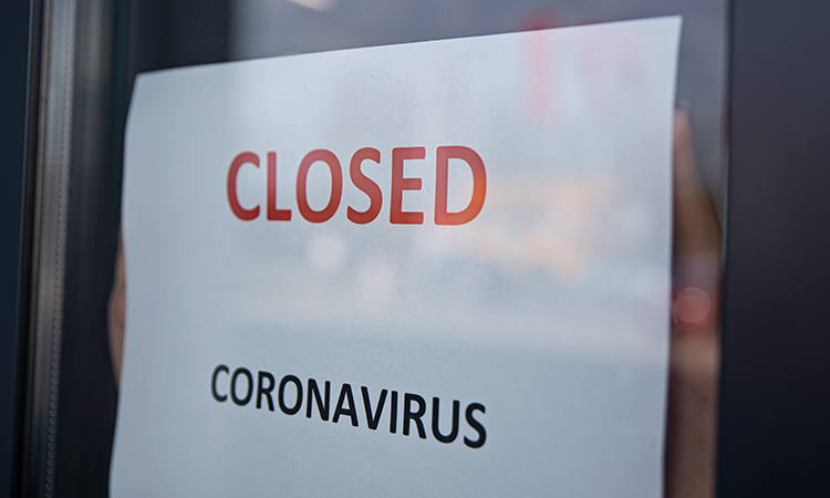 Woman hangs a card with information about the store closing due to coronavirus on a shop window