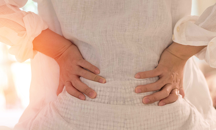 An image of a woman holding her sore back with both hands is used to illustrate the concept of low back pain syndrome.