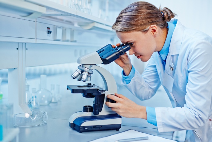 Female scientist looking through a microscope in laboratory for the sake of pain research